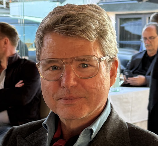 Älterer Mann mit heller Brille, grauem Sakko und rotem Halstuch